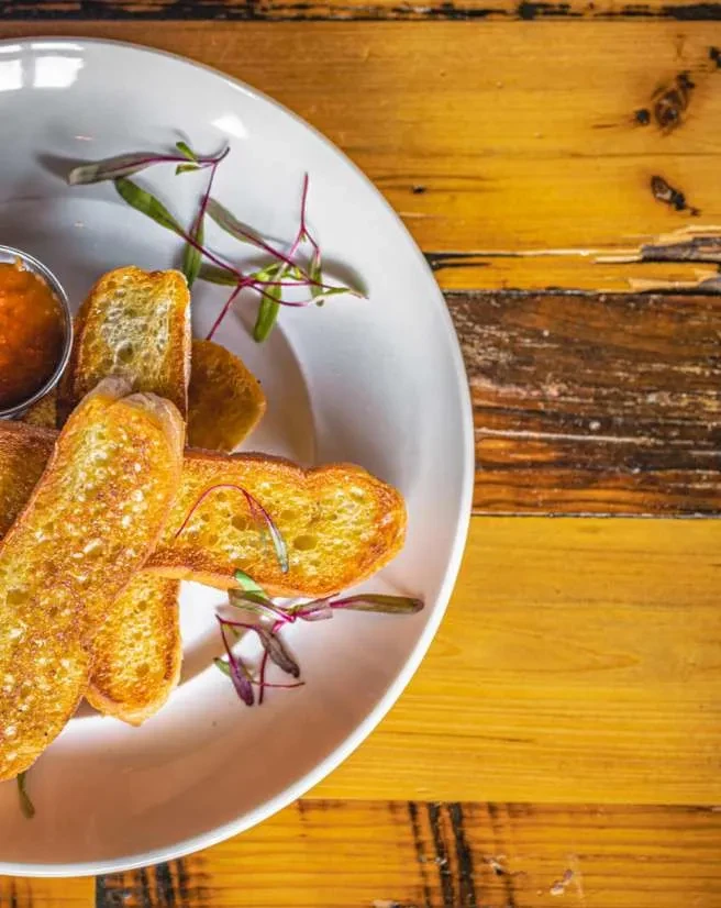 Golden-brown toasted bread, microgreens, and orange dip on a wooden table.