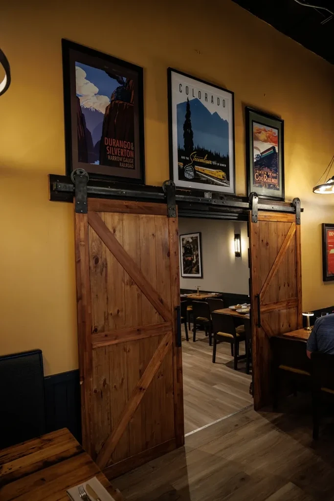 Restaurant with rustic barn doors and Colorado train-themed posters.