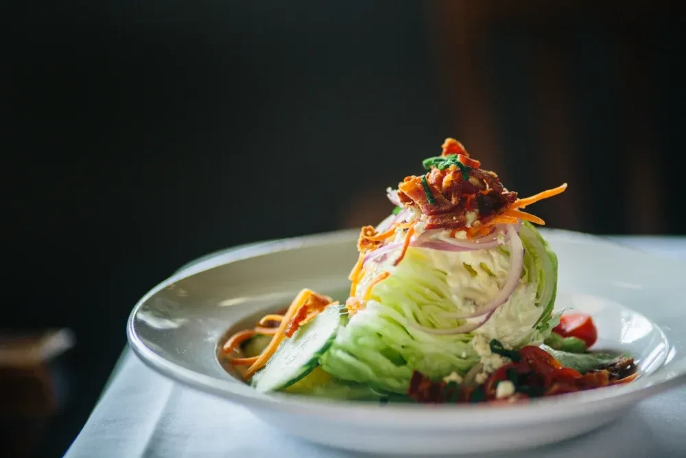Elegant wedge salad with iceberg, creamy dressing, bacon, blue cheese, and tomatoes.