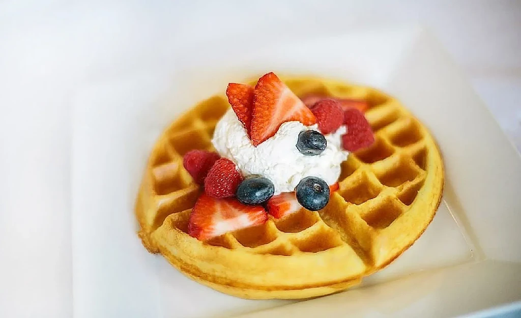 Golden waffle with whipped cream, raspberries, blueberries, and strawberry slices.