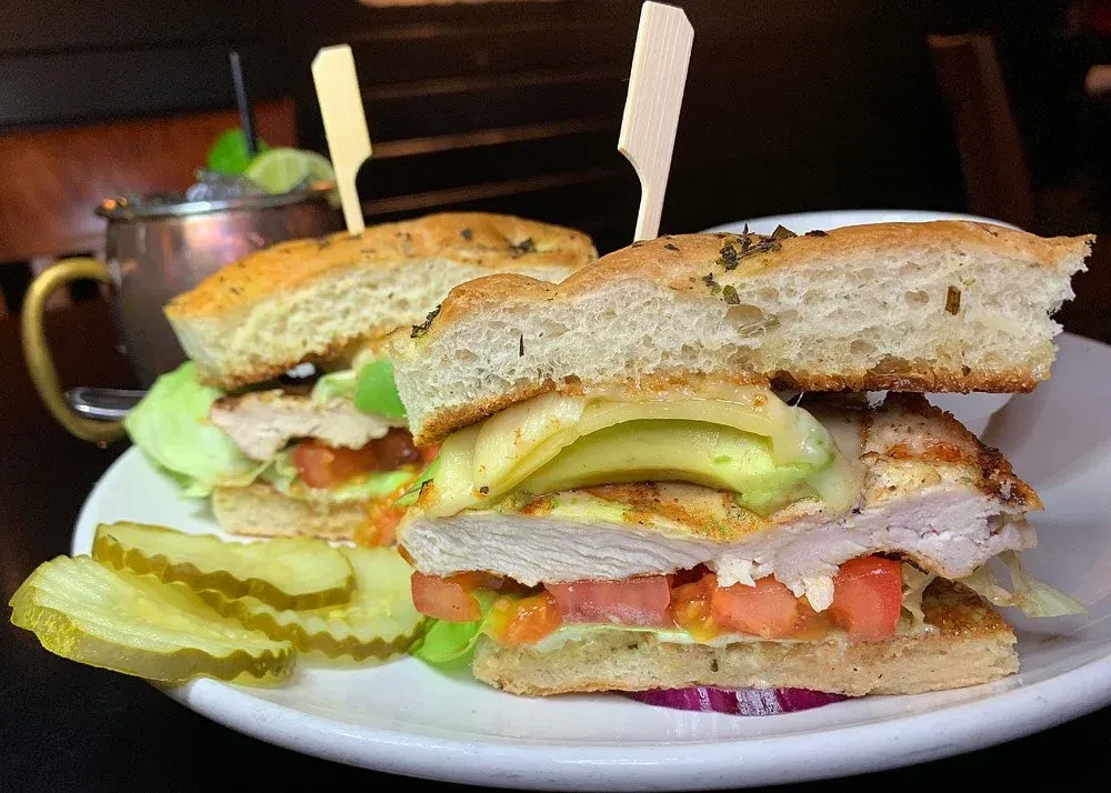 Large focaccia sandwich with chicken, avocado, cheese, and pickles.