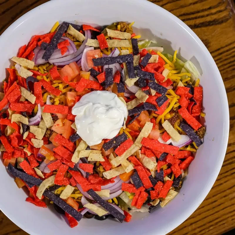 Colorful taco bowl with meat, cheese, vegetables, crispy strips, and sour cream.