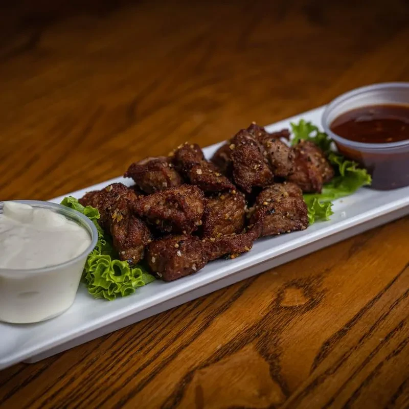 Platter of seasoned steak tips, lettuce, and two dipping sauces.