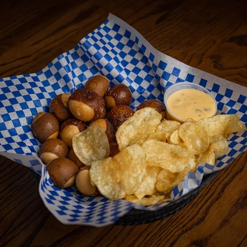 Basket of pretzel bites, chips, and cheese dip on wooden table.