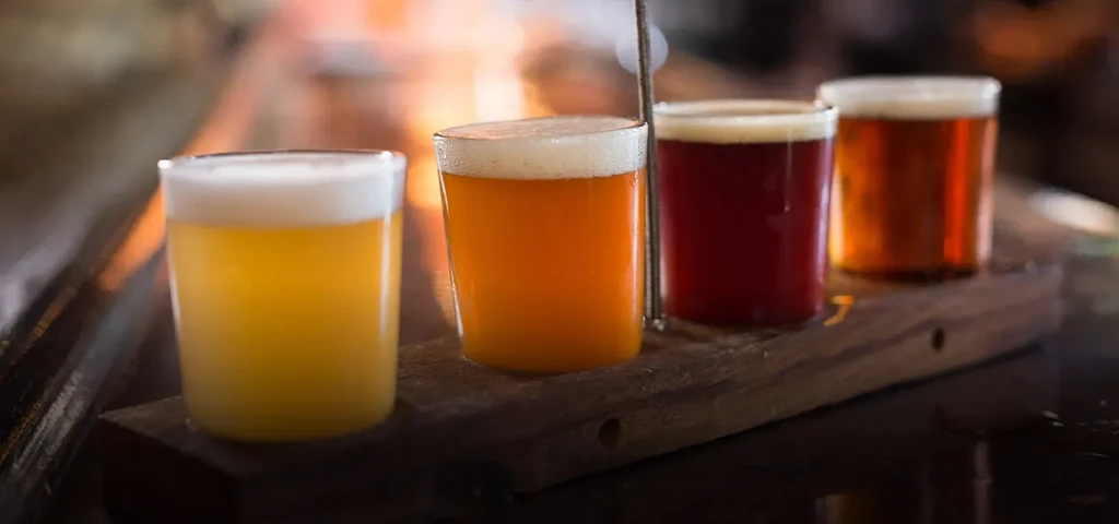 Four distinct foamy beers on a rustic wooden flight paddle.
