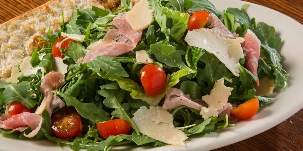 Arugula salad with cherry tomatoes, prosciutto, and Parmesan cheese.
