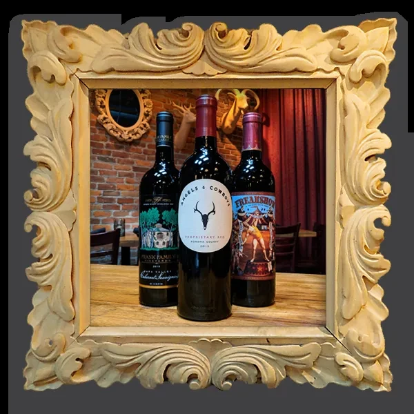 Three labeled red wine bottles in an ornate wooden frame.