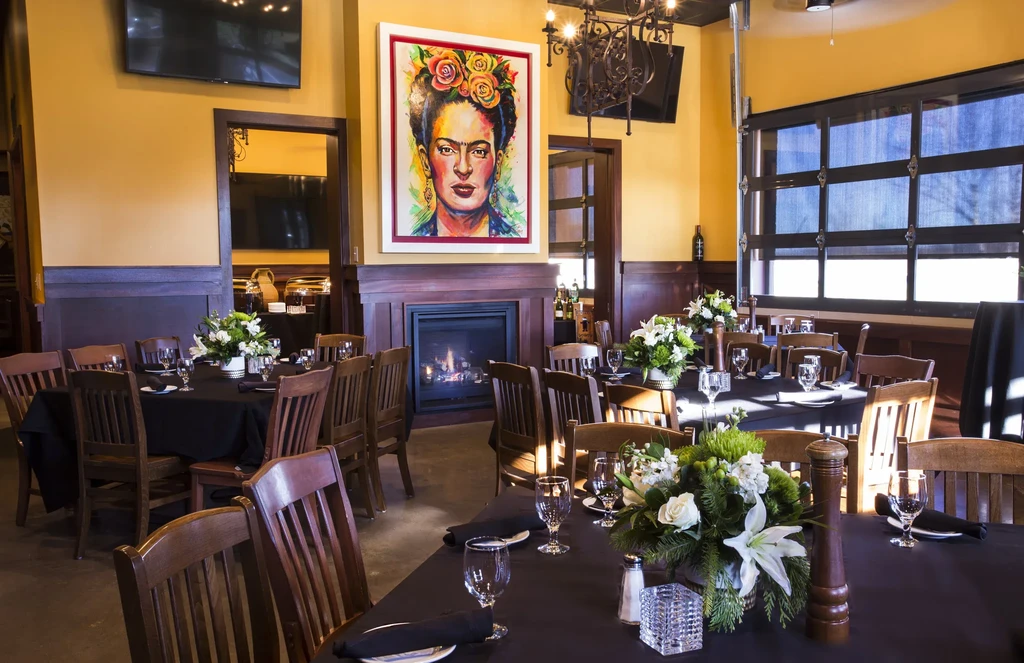 Dining room with set tables, fireplace, and Frida Kahlo portrait.
