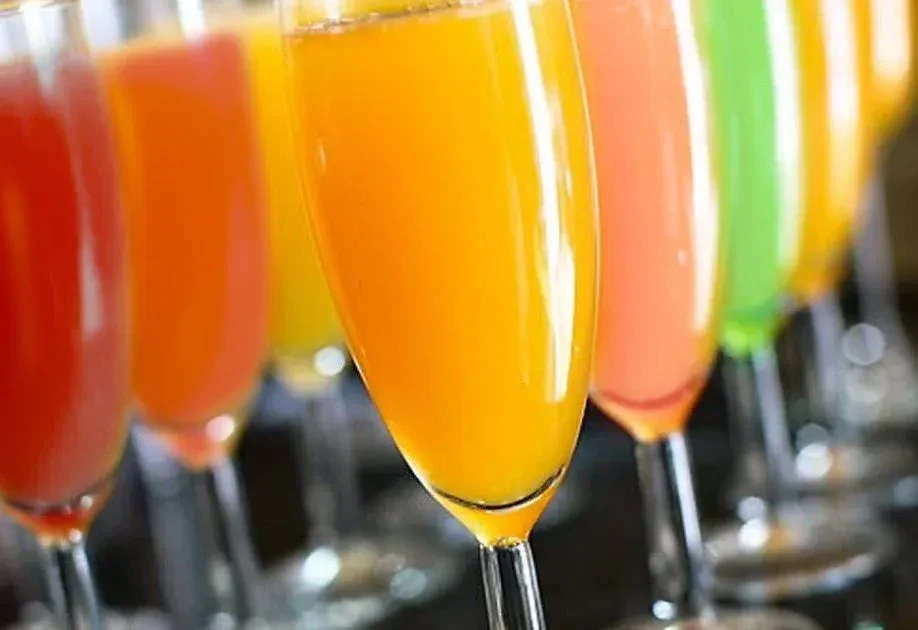 Row of colorful beverages in champagne flutes, focus on orange.