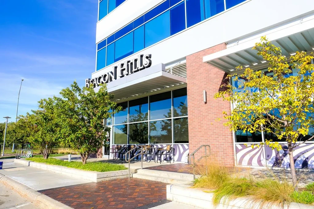 "Beacon Hills" building: blue glass, brick, patterned wall, and green landscaping.