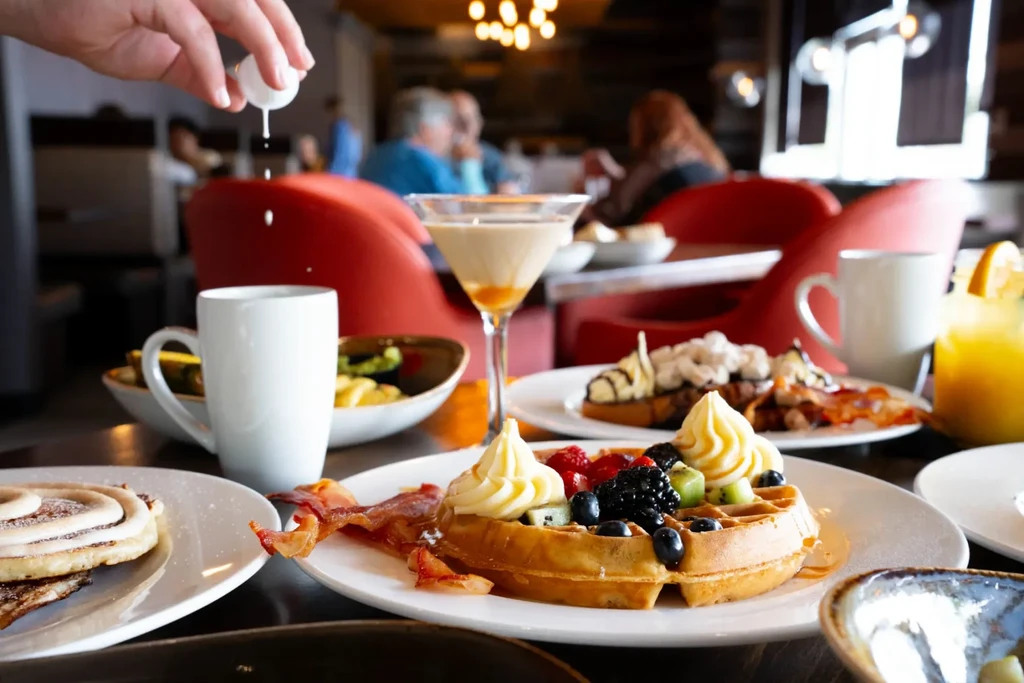 Restaurant table with waffle, bacon, coffee, and a lavish brunch.