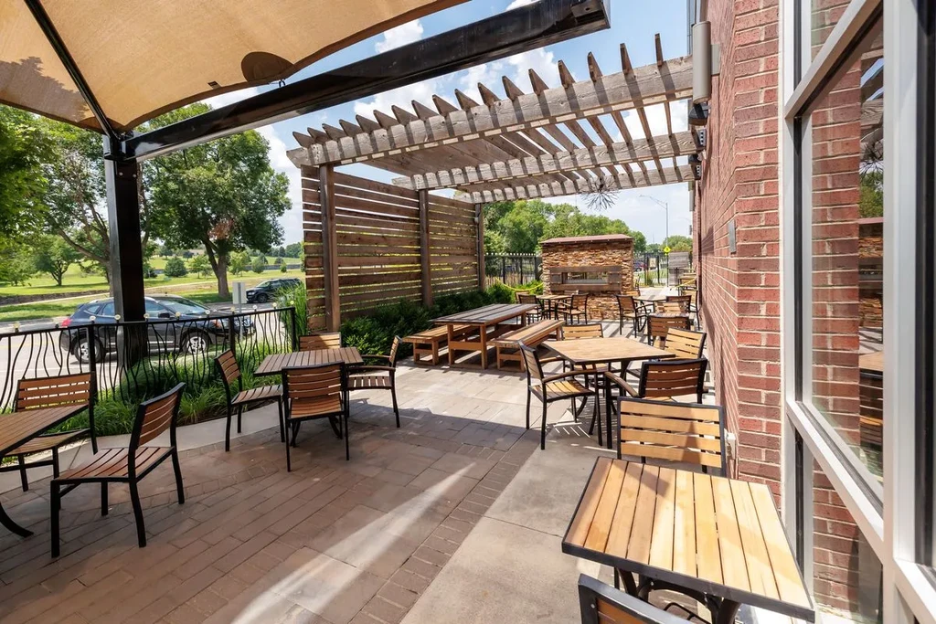 Empty outdoor restaurant patio with tables, pergola, and brick oven.