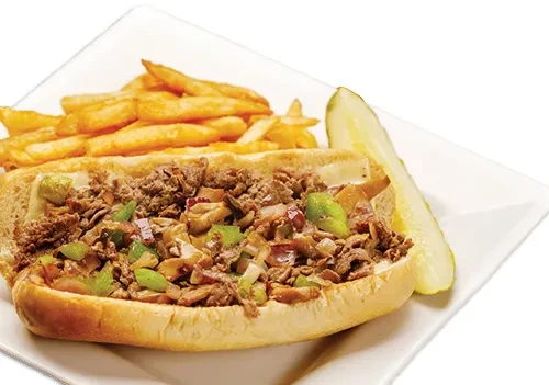 Cheesesteak-style sandwich with peppers, french fries, and a pickle spear.