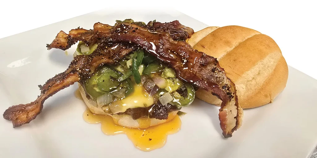 Close-up of gourmet burger with melted cheese, jalapeños, onions, and crispy bacon.
