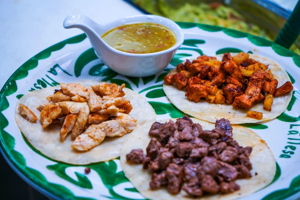 Three tacos with distinct fillings and salsa on a decorative plate.