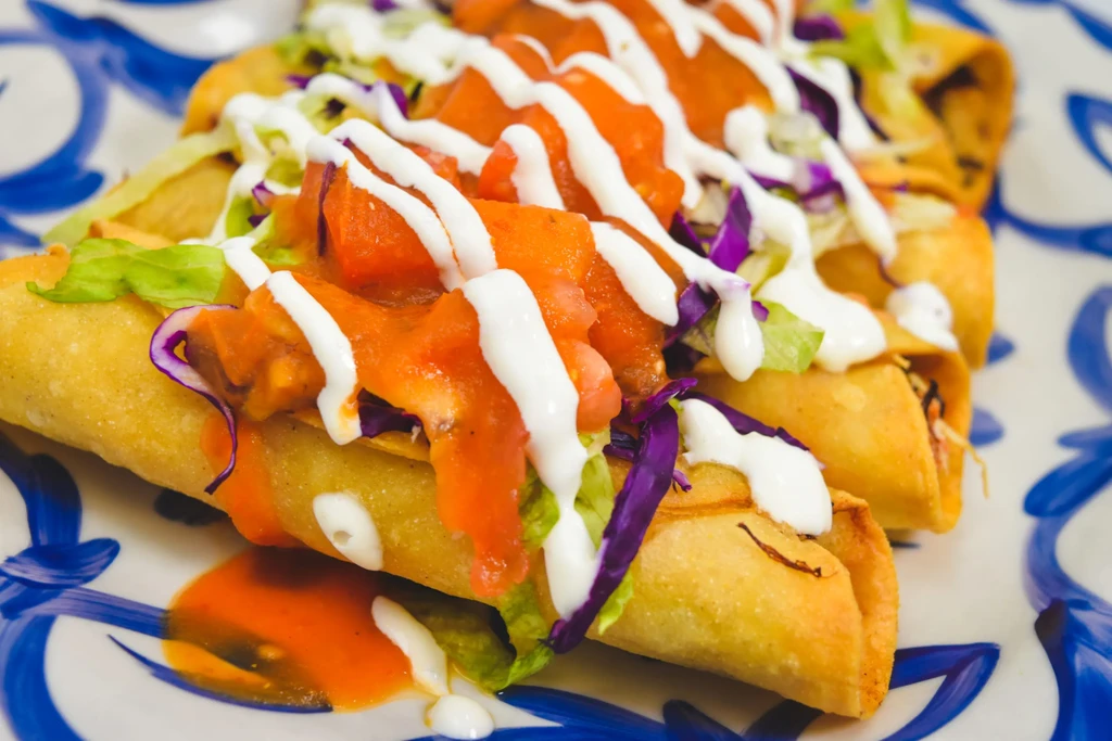Crispy golden-fried taquitos topped with lettuce, cabbage, salsa, and crema.