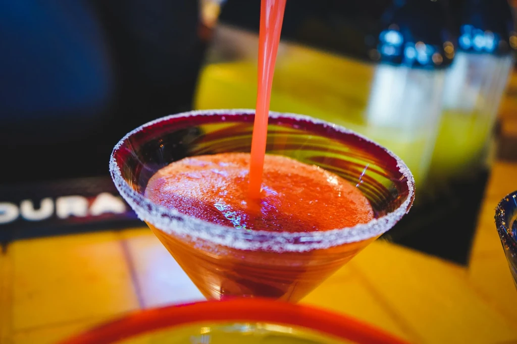 Foamy red/orange frozen drink poured into striped martini glass with sugared rim.
