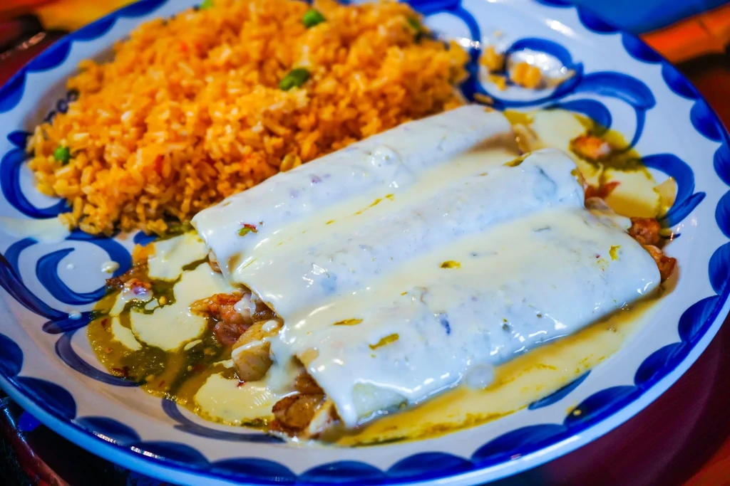 Three creamy white sauce enchiladas with orange Mexican rice on plate.