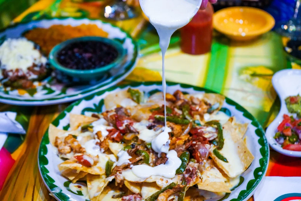 Loaded nachos with white sauce pouring, melted cheese, and fresh toppings.
