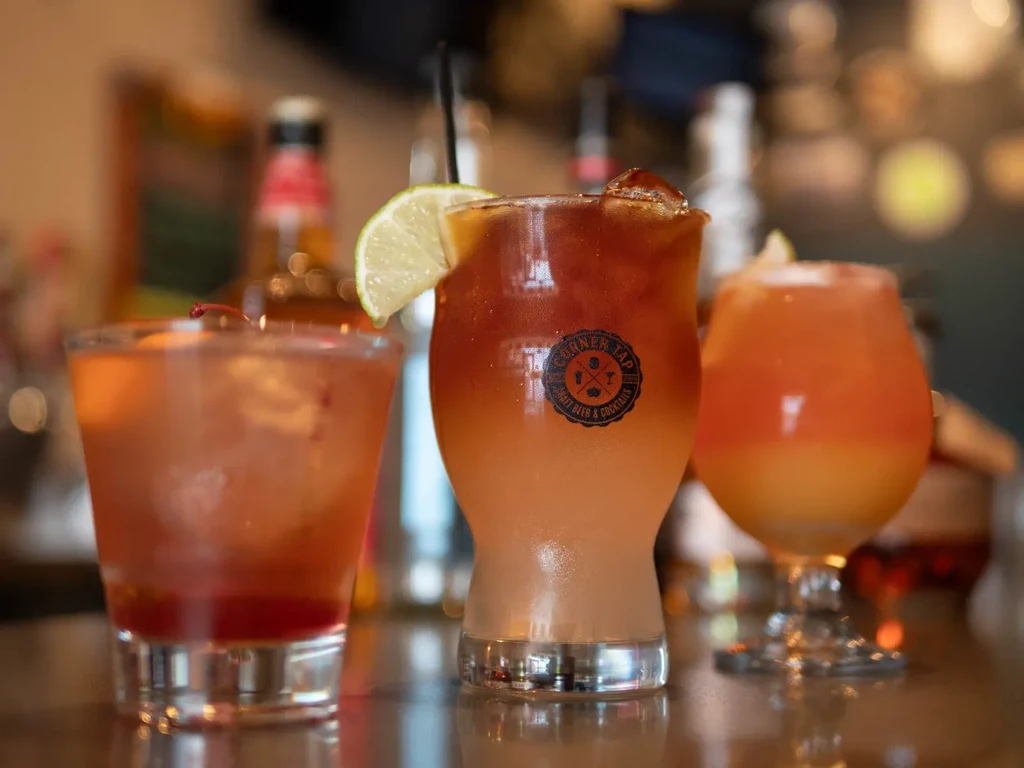 Three cocktails on a reflective bar counter with a Garner Tap logo.