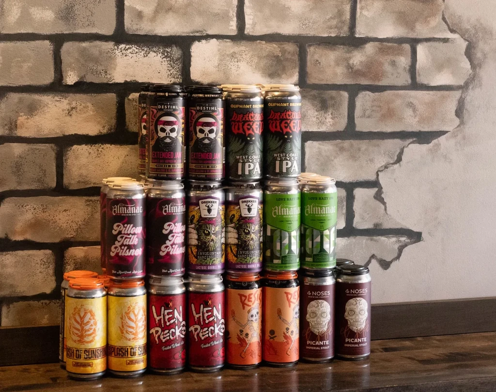 Pyramid of 22 diverse beer cans on wood, distressed brick background.