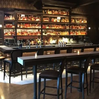 Elegant, well-stocked bar with illuminated whiskey bottles and bar stools.