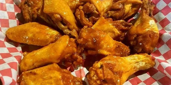 Close-up of golden-brown glazed chicken wings in a red checkered basket.