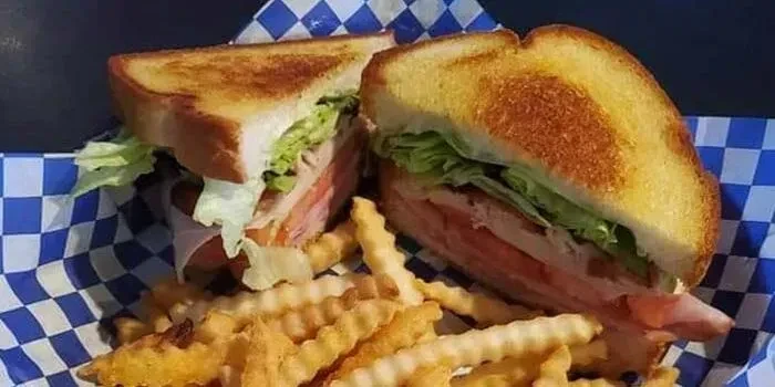 Toasted deli sandwich, cut diagonally, with crinkle-cut french fries.