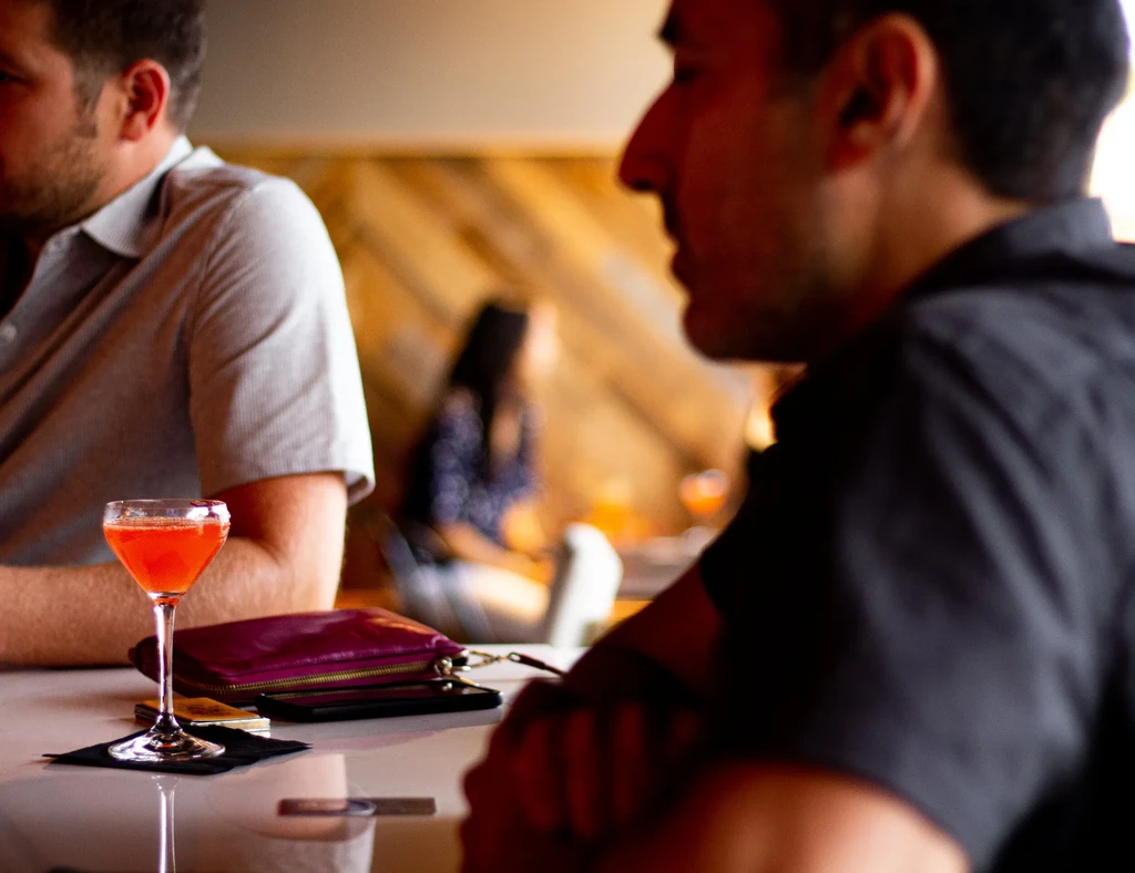 Reddish-orange cocktail on a white table surrounded by blurred people.
