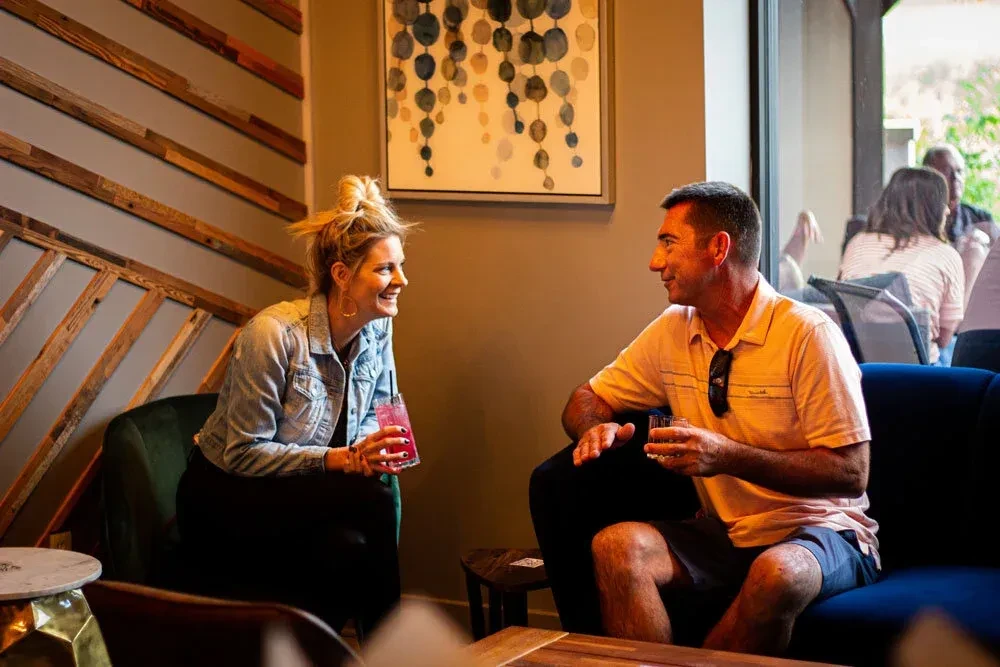 Man and woman smiling, conversing over drinks in a modern restaurant.