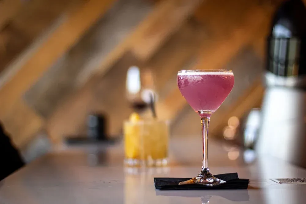 Vibrant pink cocktail with white frothy head on a modern bar.
