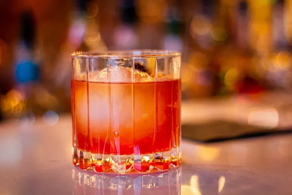 Close-up Old Fashioned cocktail with spherical ice, garnish, and warm bokeh background.