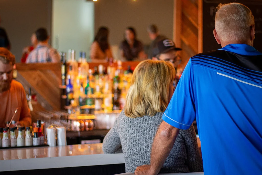 Man and woman viewed from behind at a bar, liquor bottles.