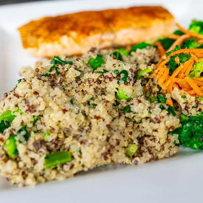 Healthy plate with salmon, tricolor quinoa, greens, broccoli, and carrots.