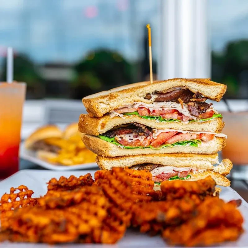 Stacked club sandwich with bacon, sweet potato fries, and orange drink.