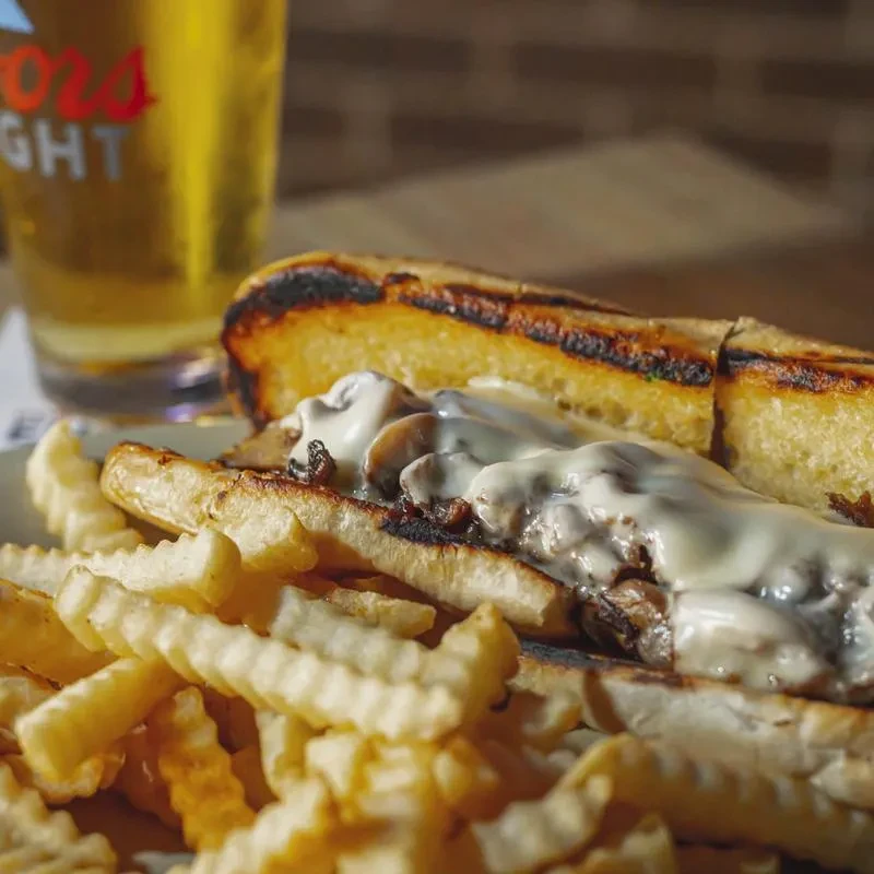 Cheesesteak with melted cheese, mushrooms, crinkle-cut fries, and beer.