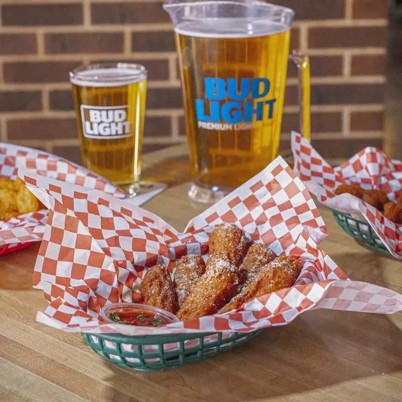 Parmesan chicken wings, red dipping sauce, and Bud Light beer on a table.