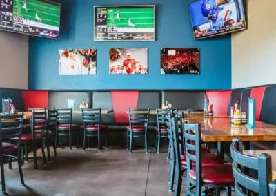 Restaurant interior with blue-green walls, red seating, and TVs showing football.