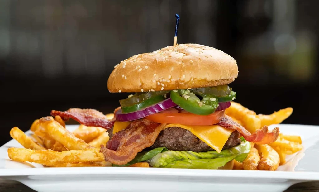 Stacked burger with cheese, bacon, jalapeños, and golden fries.