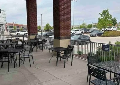 Empty outdoor patio with black tables and chairs next to a parking lot.