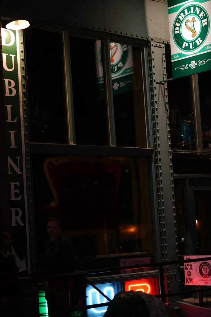 Industrial Dubliner Pub facade at night, green signs, neon lights.