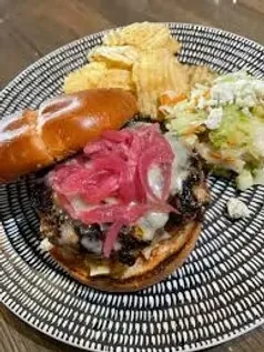 Gourmet open-faced burger, pickled onions, chips, coleslaw on patterned plate.