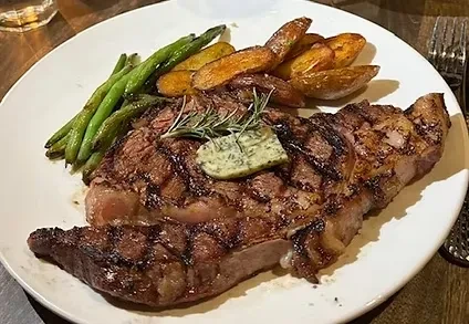 Top-down view of grilled steak, herbed butter, green beans, roasted potatoes.