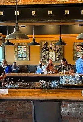 Interior of a rustic bar with patrons, wood counter, and wine rack.