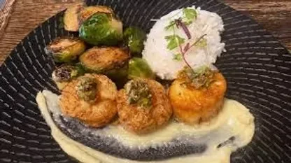 Plated seared scallops, Brussels sprouts, and rice on a dark plate.