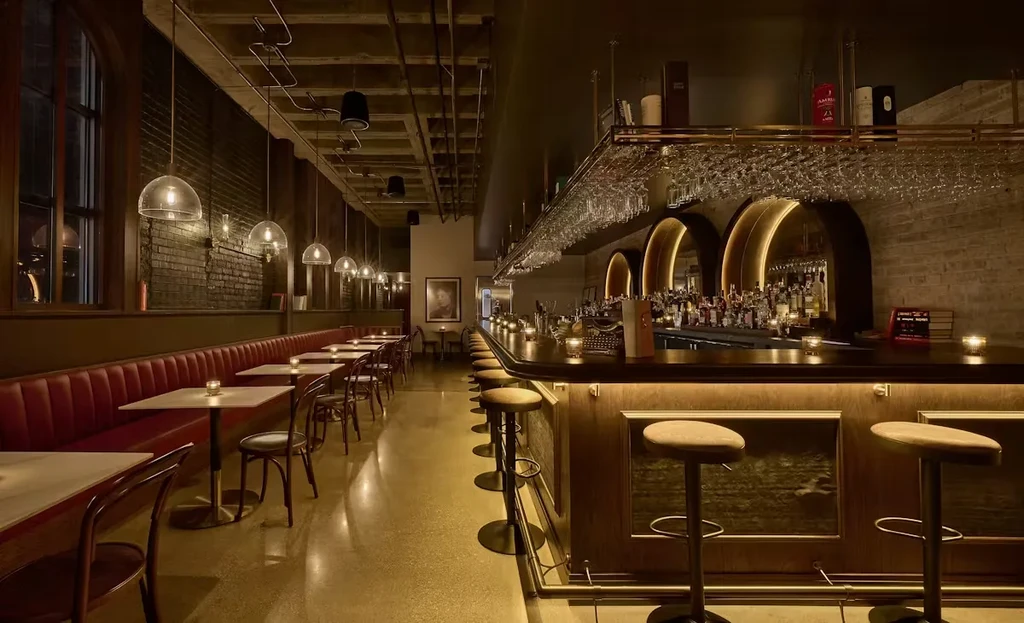 Dimly lit, industrial-chic bar with red banquette and dark wood bar.