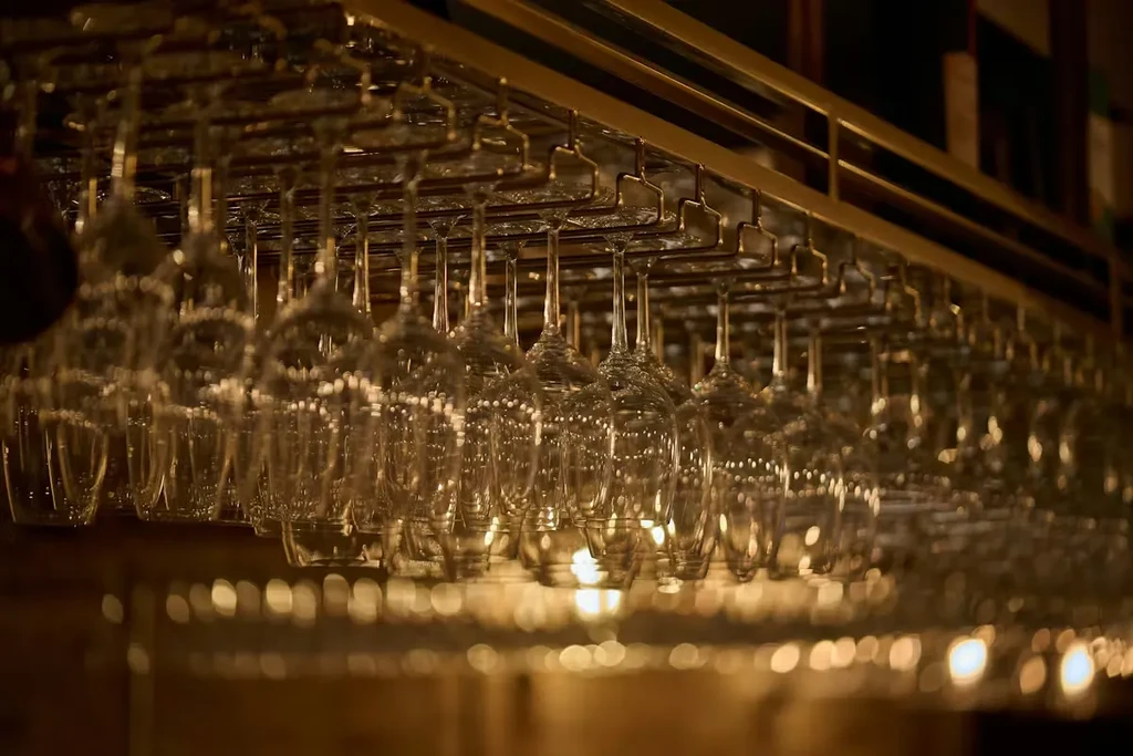 Clear glass wine glasses hang upside down on a gold rack.