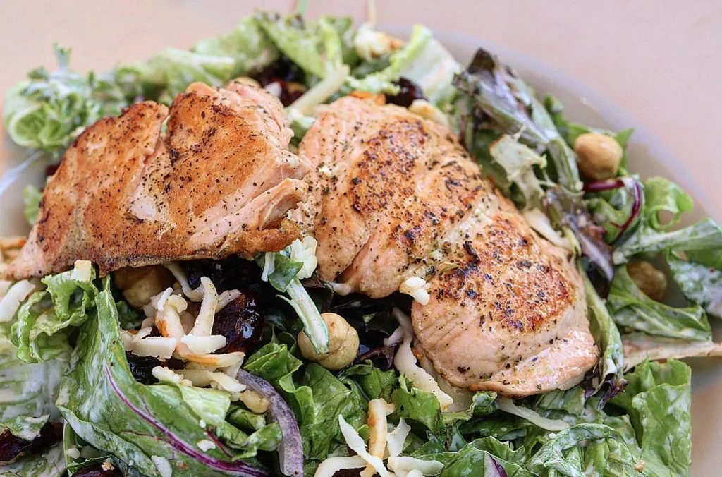 Two flaky salmon fillets on a vibrant mixed green salad.