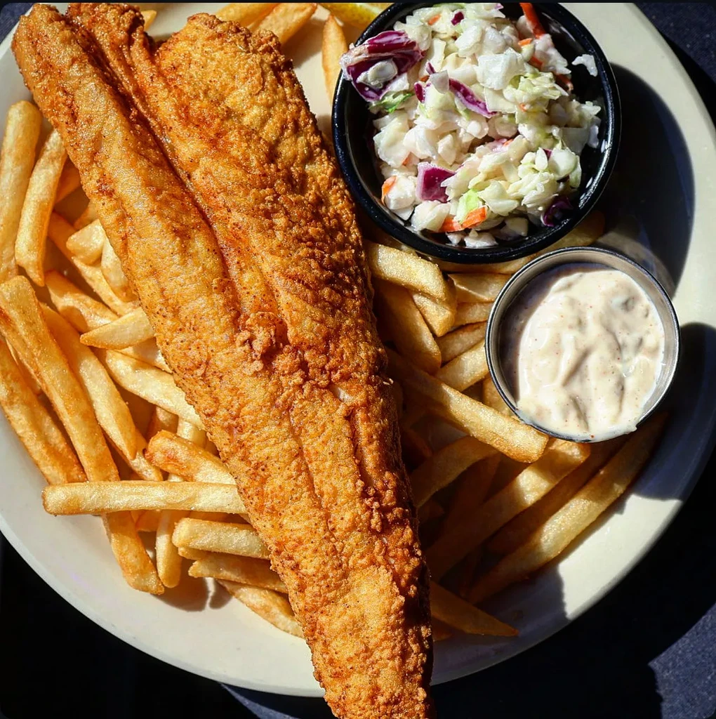 Fried fish fillet, french fries, coleslaw, and tartar sauce on a plate.