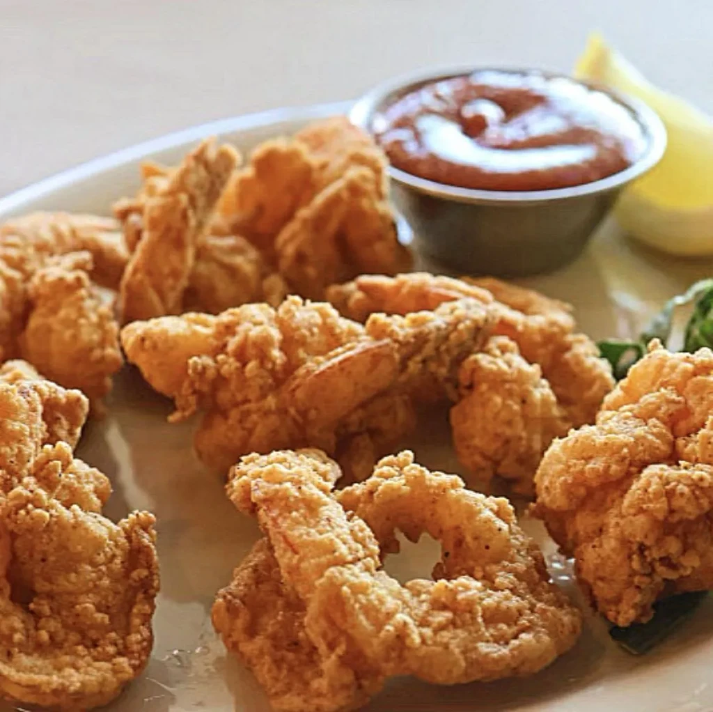 Golden fried seafood with a lemon wedge and red dipping sauce.